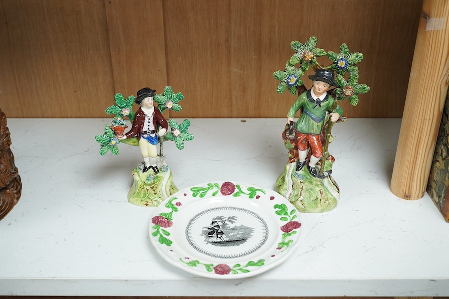 Two early 19th century Walton pearlware figures, the first a man holding a basket flowers, the second a cider costrel, tallest 19.5cm, together with a pearlware nursery plate (3). Condition – some restoration otherwise f